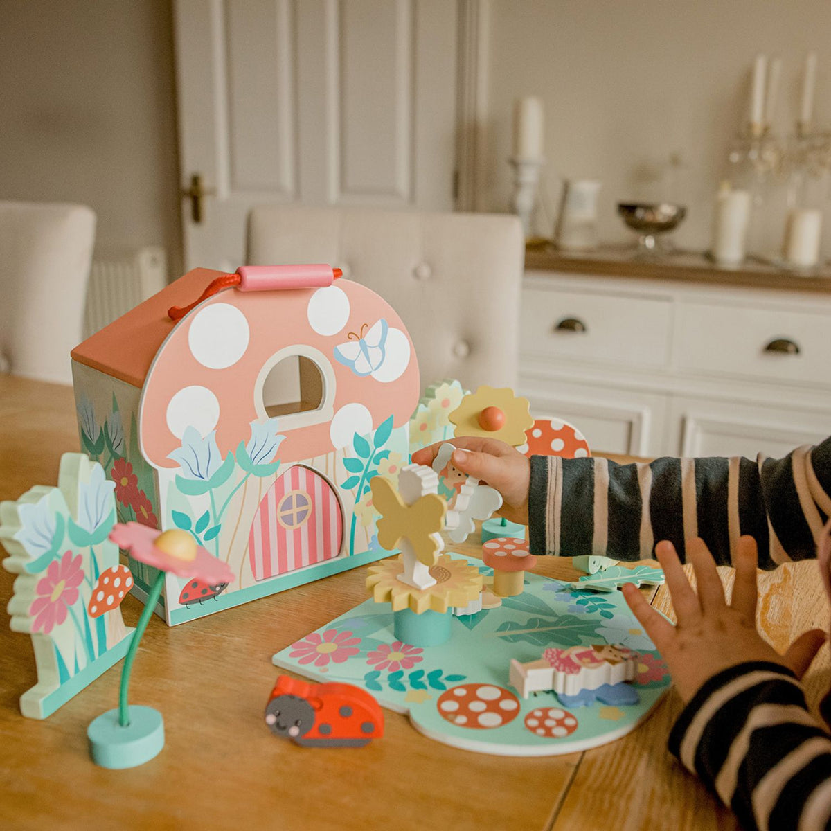 A close-up shot of a young child’s hands placing a wooden fairy figure next to  the open house, illustrating fine motor control and small-world play.