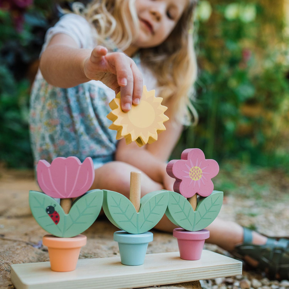 close-up shot of a toddler’s hands carefully balancing the smallest painted wooden flower pot on top of the stack, capturing the concentration and fine motor precision encouraged by the toy.