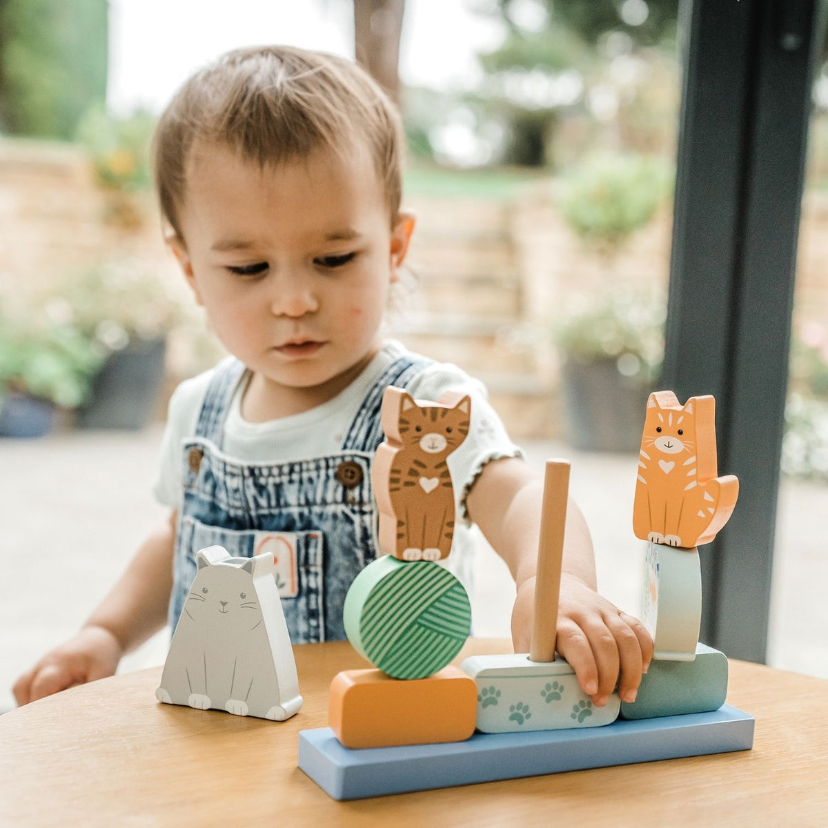 A close-up shot of a toddler’s hands carefully aligning a chunky wooden cat block onto the central peg, capturing fine motor control and concentration.
