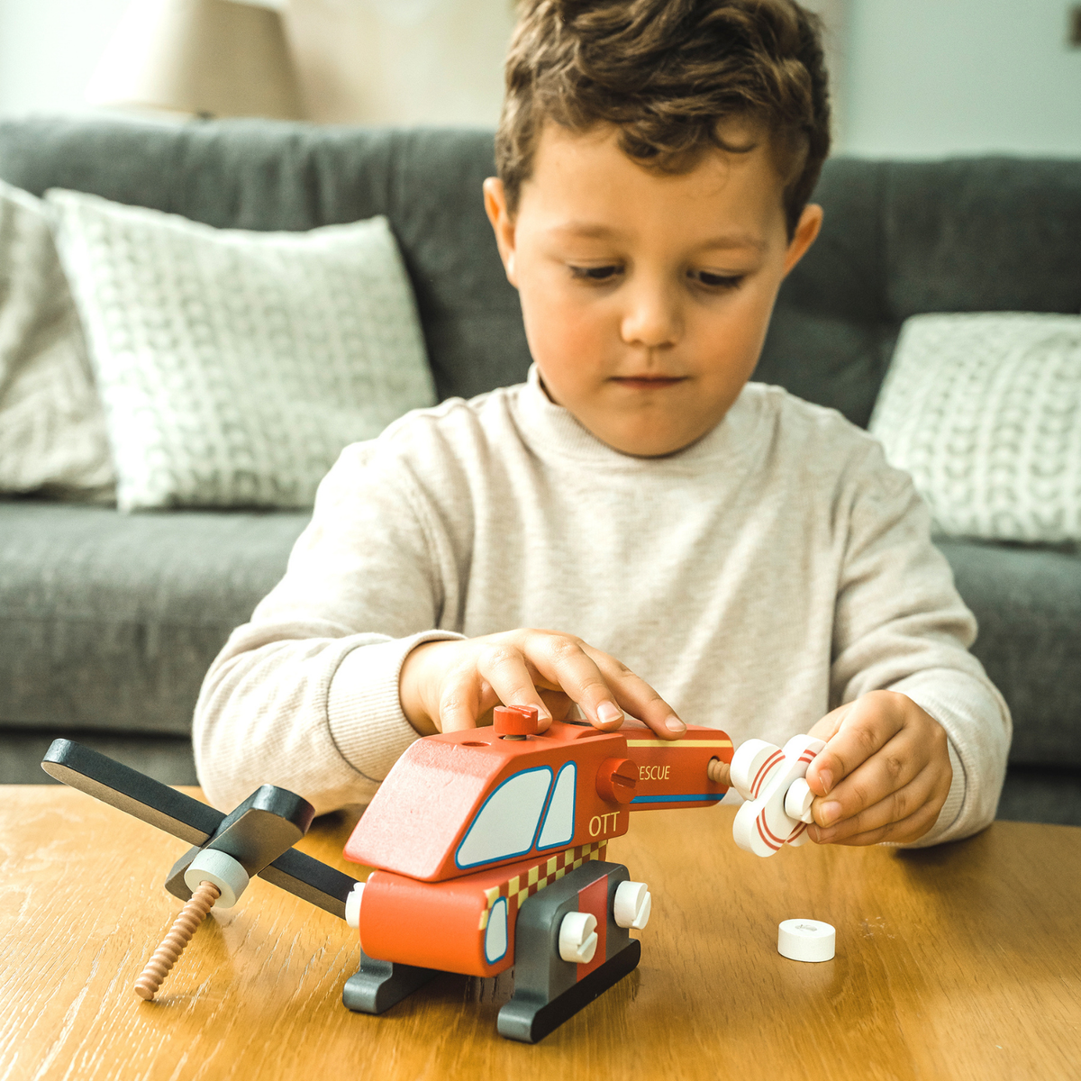 lose-up shot of a young child’s hands carefully connecting the modular wooden body pieces of the helicopter on a wooden play table, capturing concentration and fine motor focus.
