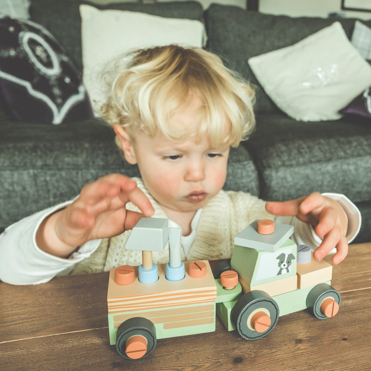 A close-up shot of a young child’s hands using the wooden screwdriver to fasten a yellow wheel onto the tractor base on a low wooden play table, capturing fine motor focus.