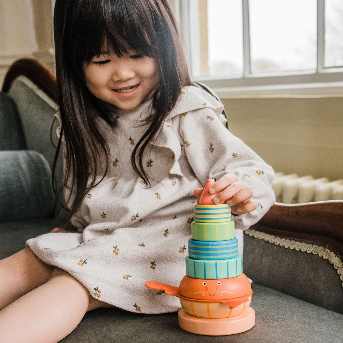 A close-up shot of a toddler’s small hands carefully sliding the final wooden piece onto the central wooden post, illustrating fine motor control and concentration.