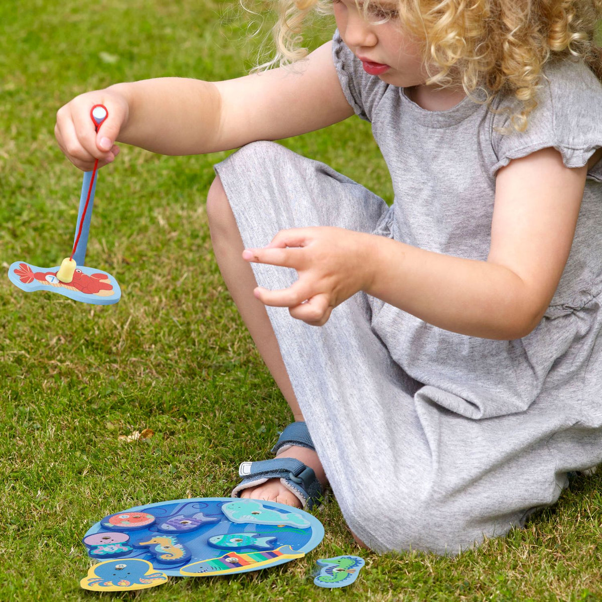 A close-up shot of a young child’s hand carefully steadying the wooden magnetic fishing rod to hook a floating sea turtle piece, illustrating fine motor control and patience.