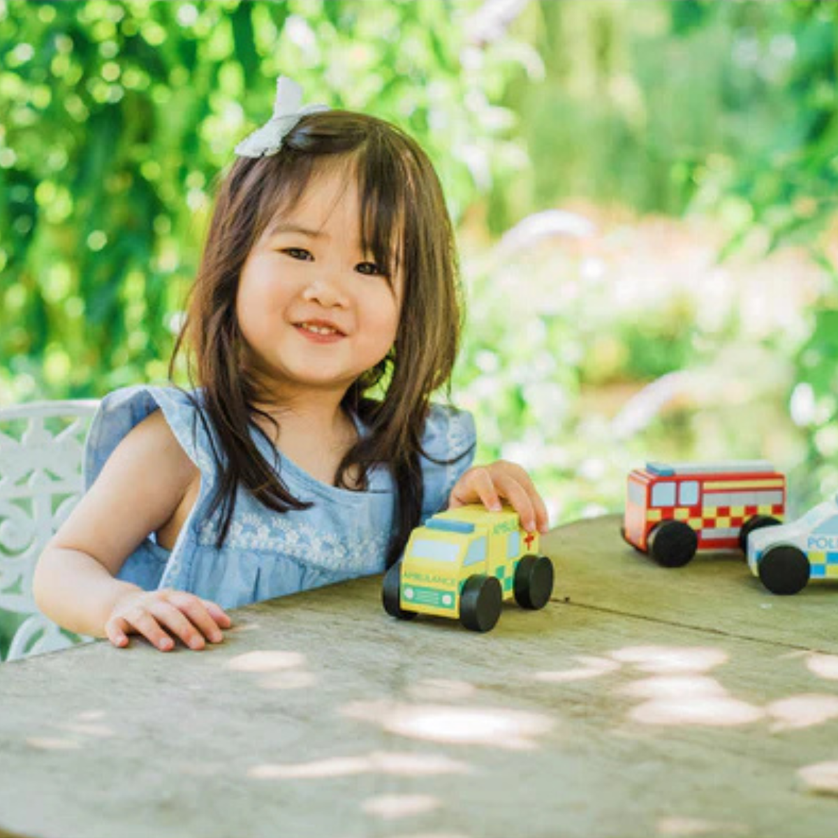 Young girl playing with the Orange Tree Toy cars, emergency vehicles outdoors on a sunny day
