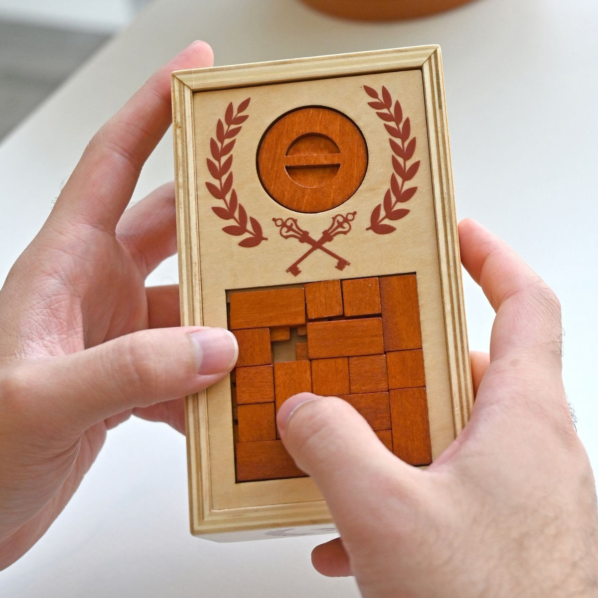 A person’s hands manipulating the sliding wooden pieces and rotating the dial to unlock the secret lid of the ancient-themed puzzle box