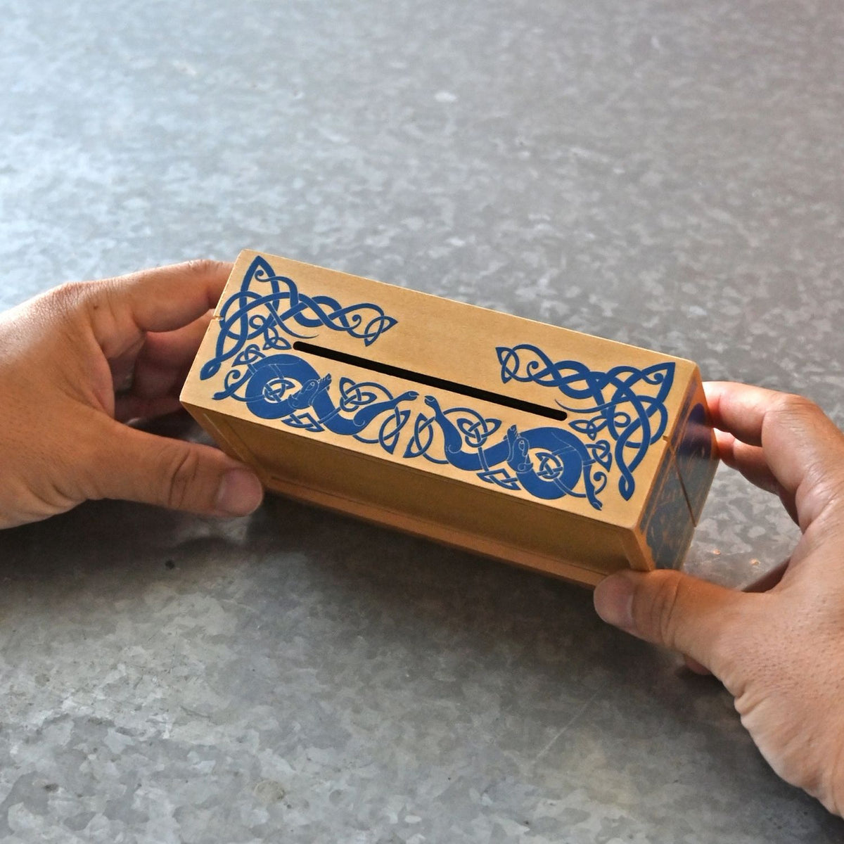 Hands manipulating the sliding wooden panels of a Viking-themed secret box to complete the sequential steps required to unlock the lid in this puzzle.